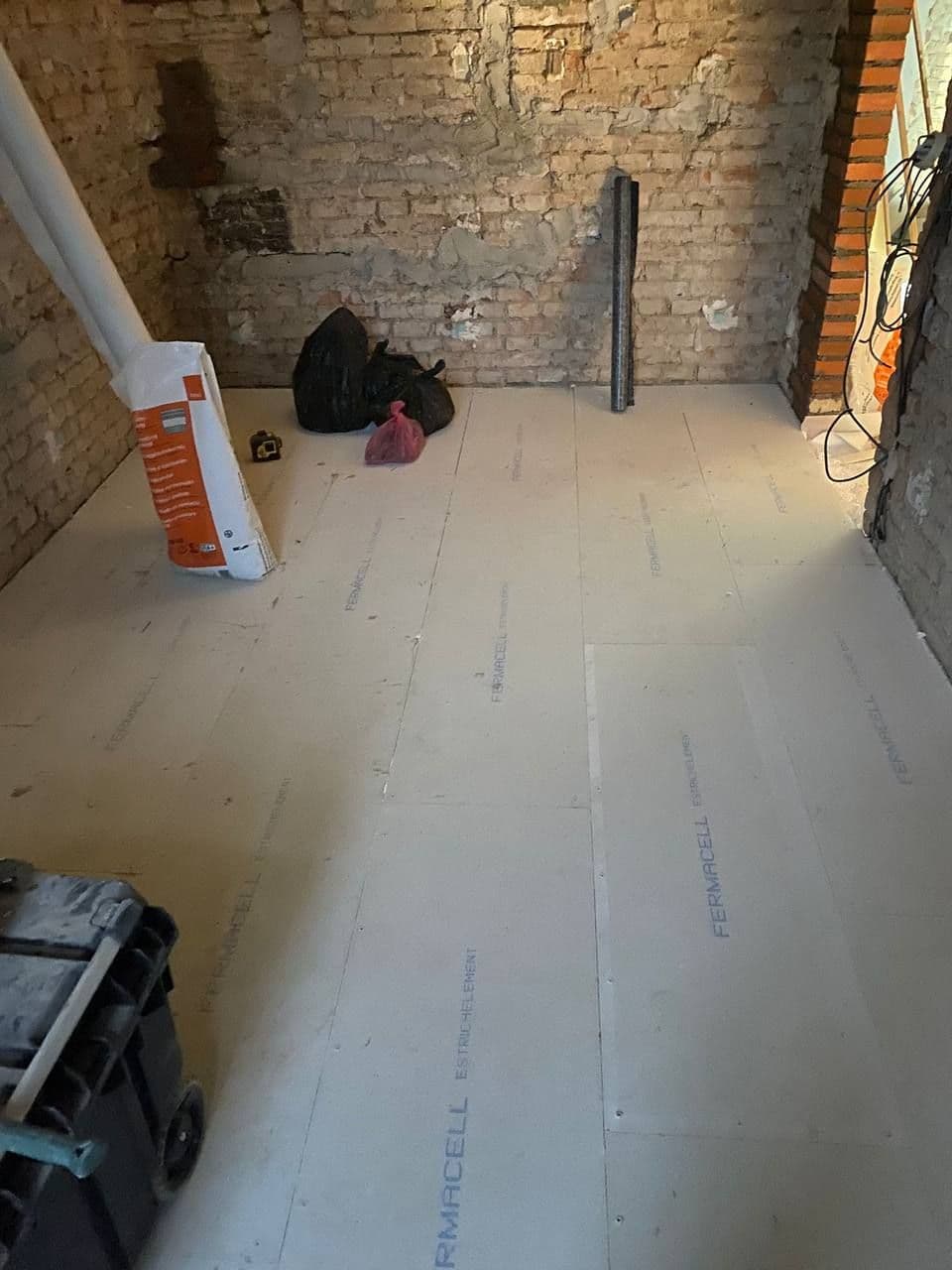 Nová podlaha ze sádrovláknitých desek suché skladby položená v místnosti s cihelnými stěnami.