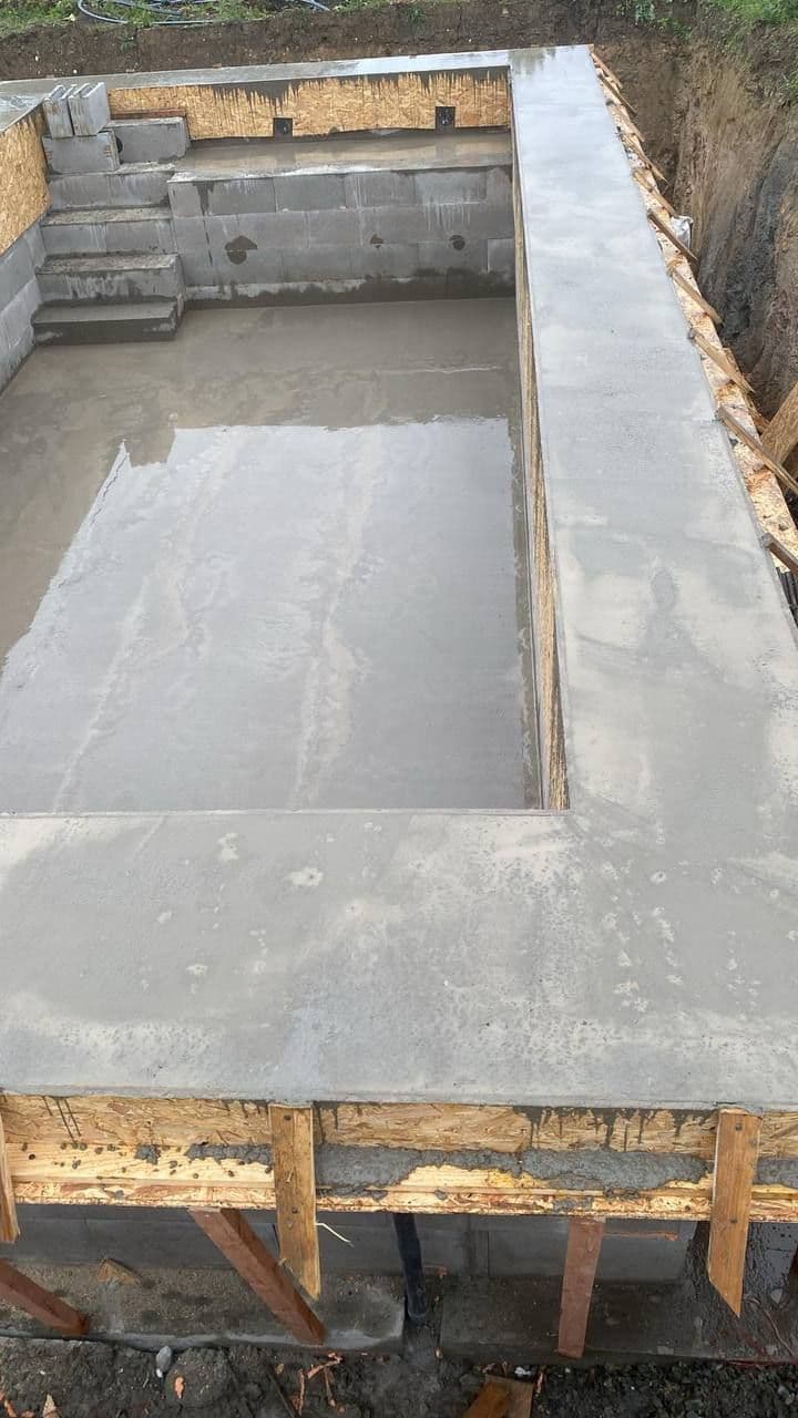 Dokončená betonová vana bazénu se schody v čele a vybetonovanou obrubou kolem okraje.